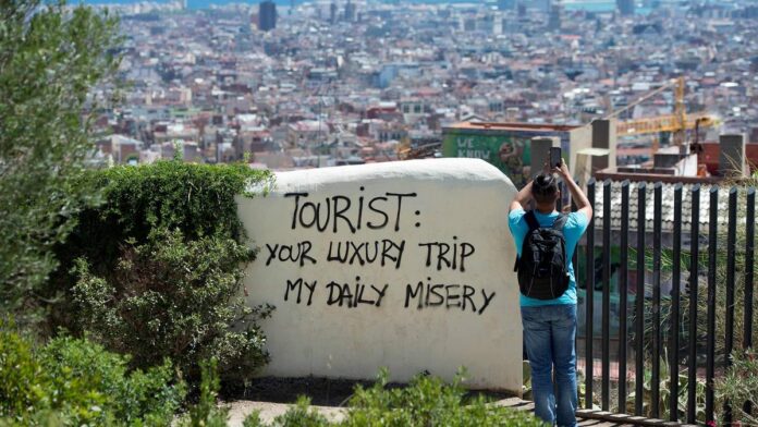 En turist tar bilde av utsikten ved siden av tagging som sier "Tourist: your luxuury trip, my daily misery"